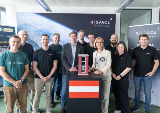 Zehn Mitarbeiter:innen von R-Space stehen mit der Landeshauptfrau von NÖ Johanna Mikl-Leitner vor dunkelblauen R-Space Plakaten. In der Mitte zwischen den Menschen steht ein schwarzer Tisch, auf dem ein Modell ihres roten  AT-Astra Satelliten und eine rot-weiß-rote Österreich Flagge zu sehen sind.